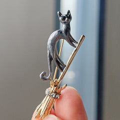 Chic and whimsical brooch featuring a cat and broom
